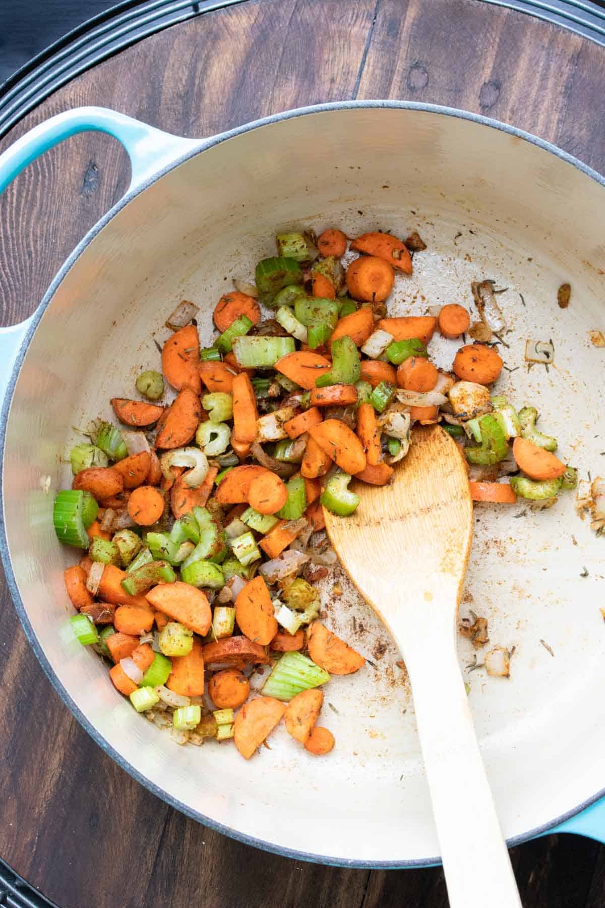 Wooden spoon mixing carrots, celery and onion in a dutch oven