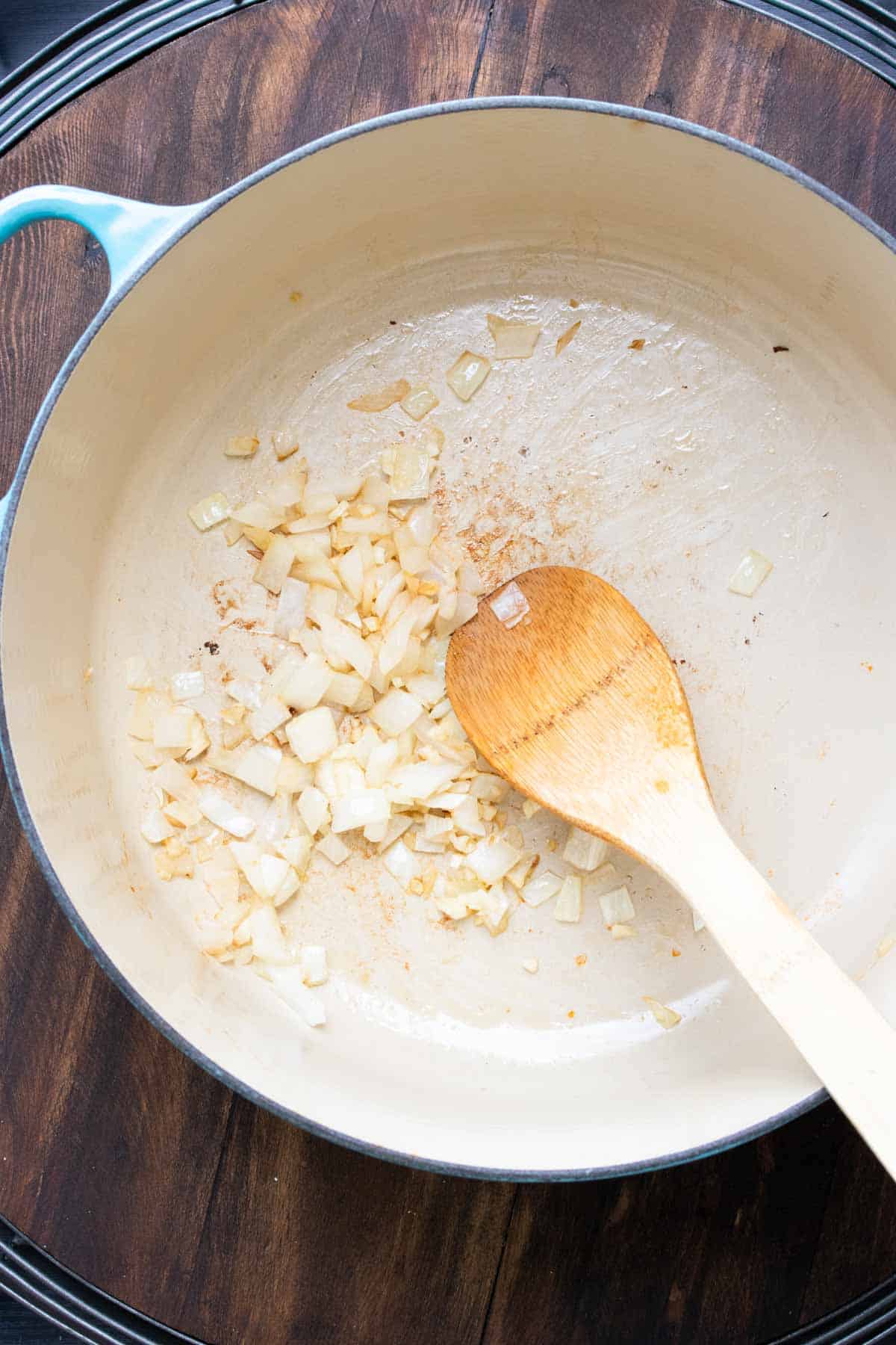 Wooden spoon sautéing onions in a dutch oven