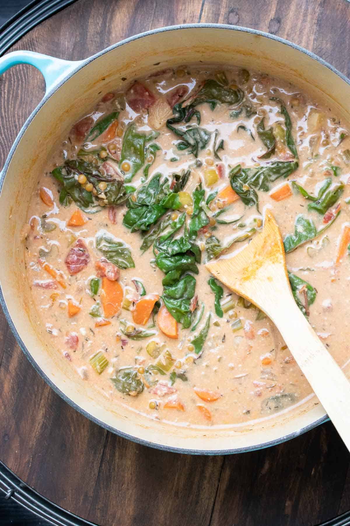 Wooden spoon stirring a creamy red lentil and veggie soup