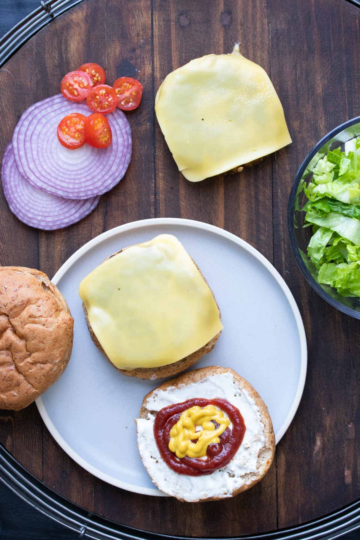 An open faced veggie burger on a bun with cheese, mayo, ketchup and mustard.