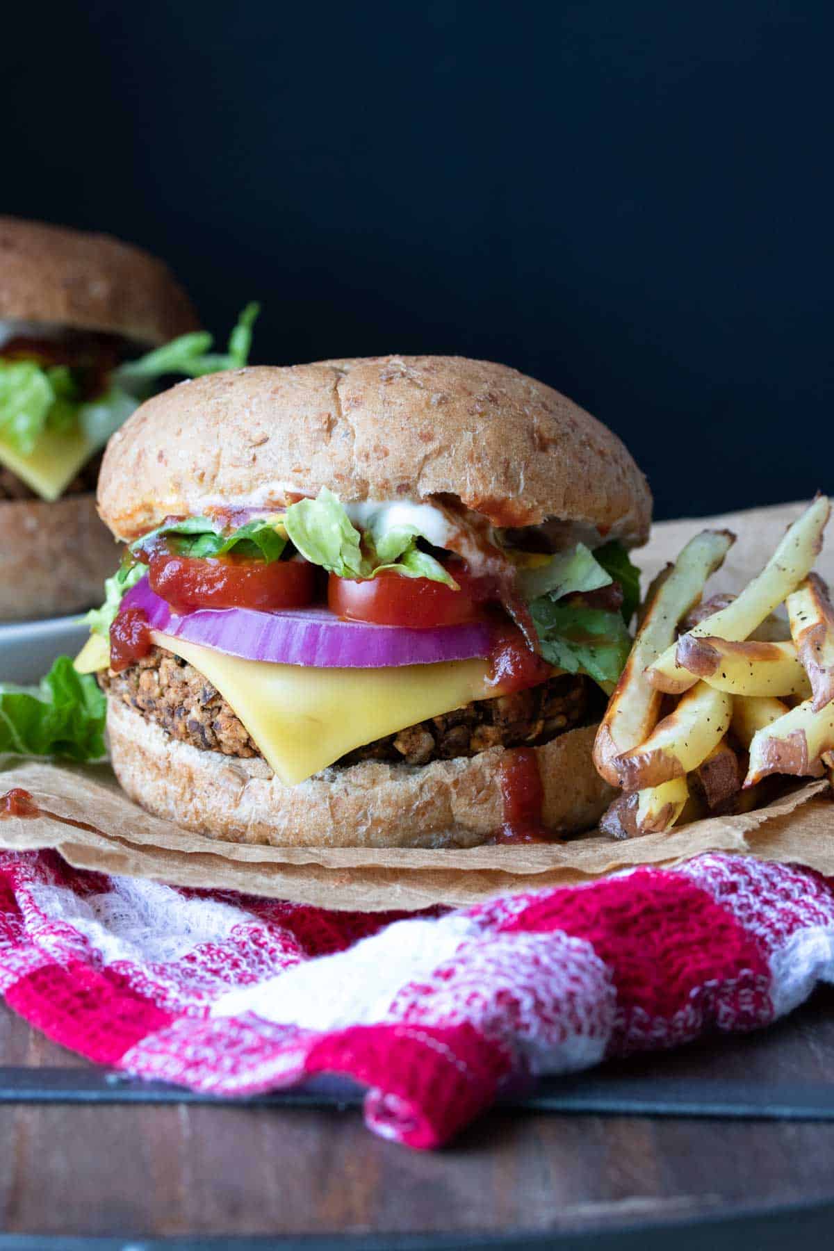 A fully loaded veggie burger on a bun next to a pile of fries