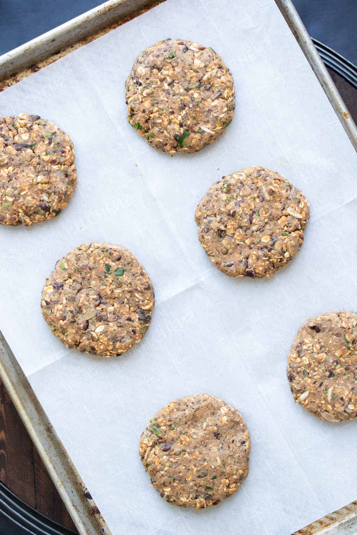 Raw veggie burgers on a parchment lined cookie sheet.