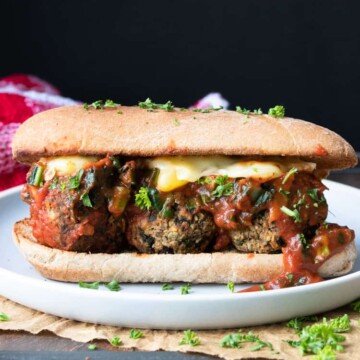 Vegan meatball sub with yellow cheese and marinara on a white plate