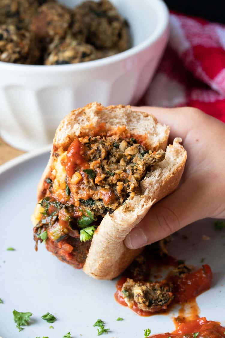 Hand holding a half eaten vegan meatball sub sandwich