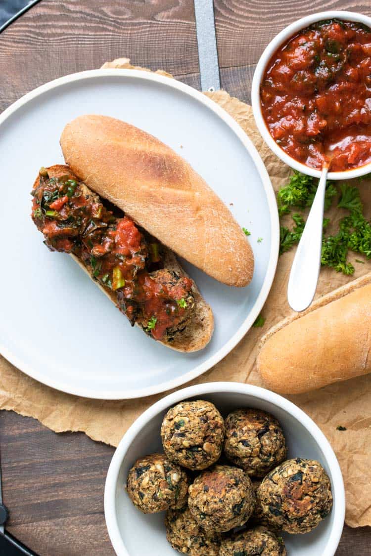 Open faced vegan meatball sub next to bowls of marinara and vegan meatballs