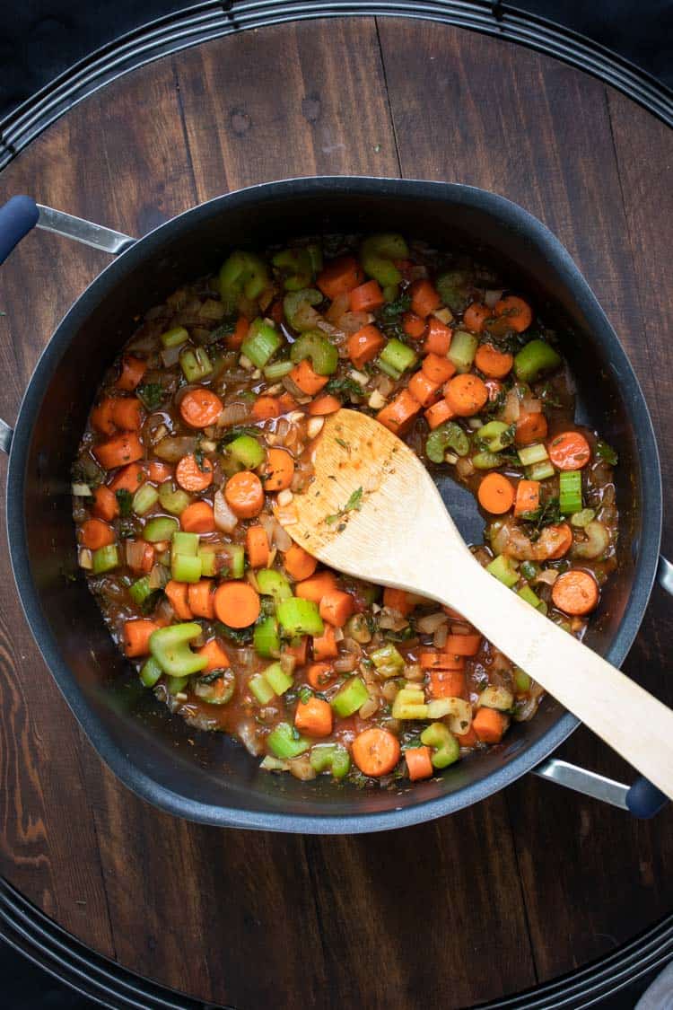 Wooden spoon mixing carrots, celery and onion cooking in a pot