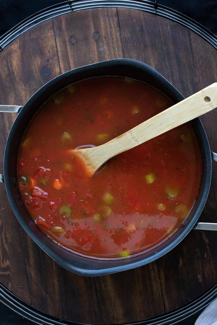 Tomato vegetable soup being stirred in a pot by a wooden spoon