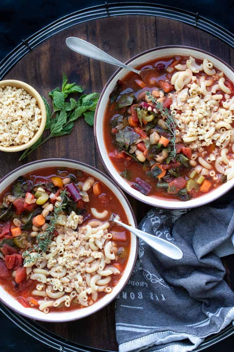 Two bowls of vegetable minestrone soup on a wooden tray