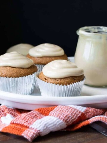 Pumpkin cupcakes with white frosting on a white plate.