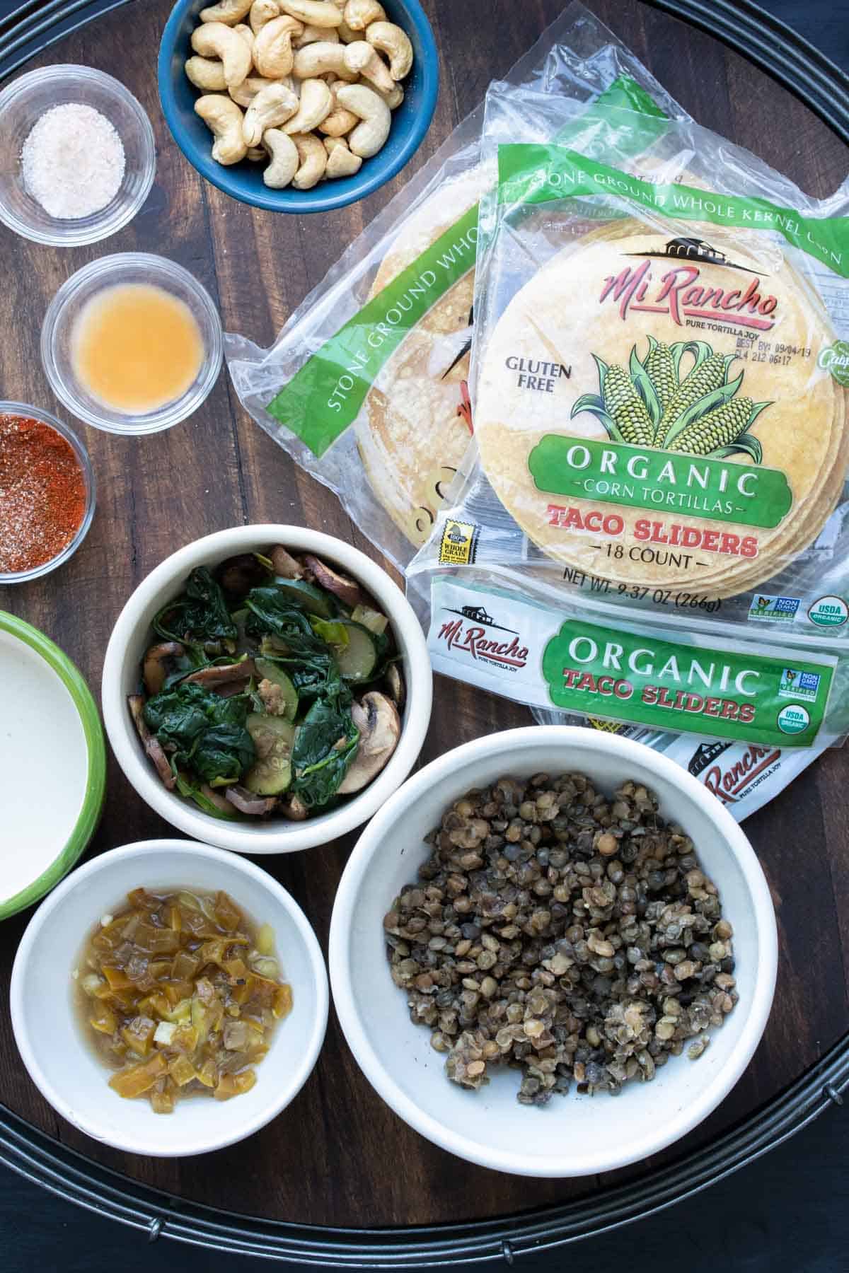 Taquito filling ingredients and bags of corn tortillas on a wooden tray