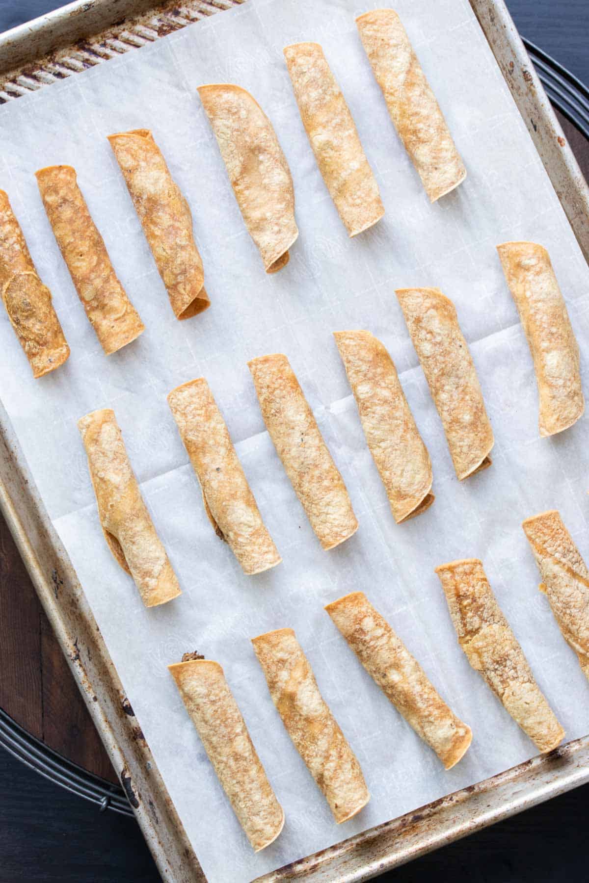 Baked taquitos on a baking sheet lined with parchment paper.