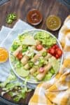 A plate with taquitos over a bed of lettuce on a wooden surface with a yellow and white towel.