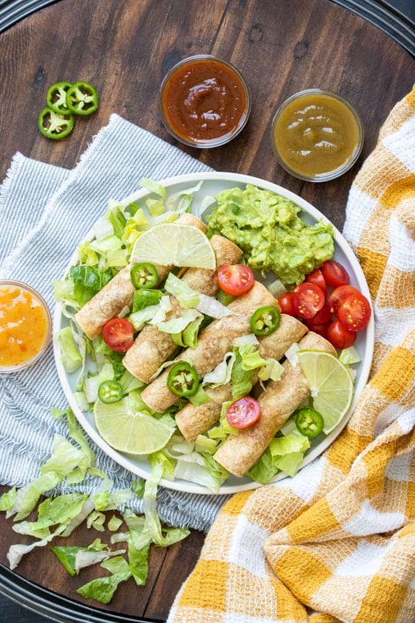 A plate with taquitos over a bed of lettuce on a wooden surface with a yellow and white towel