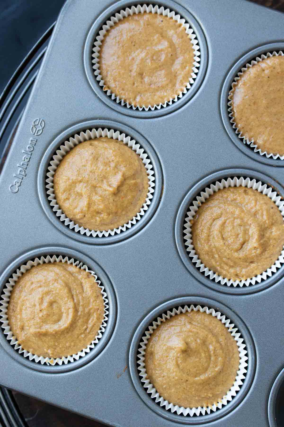 Top view of baking cups filled with pumpkin cupcake batter in muffin pan