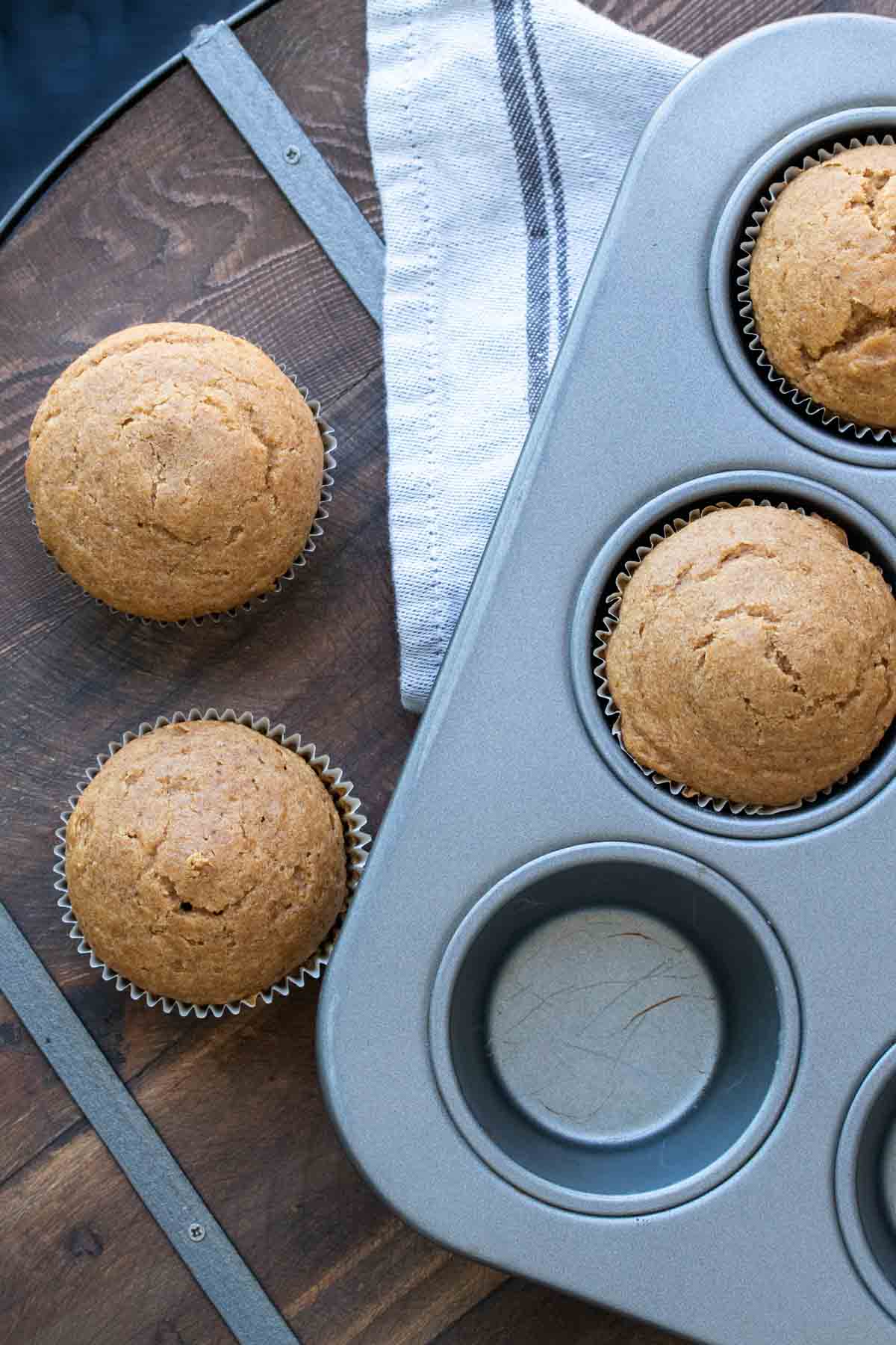 Baked pumpkin cupcakes in a muffin tin and on a wood table