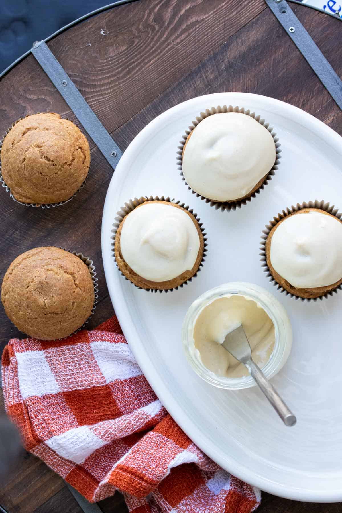 White plate with pumpkin cupcakes on it being frosted.