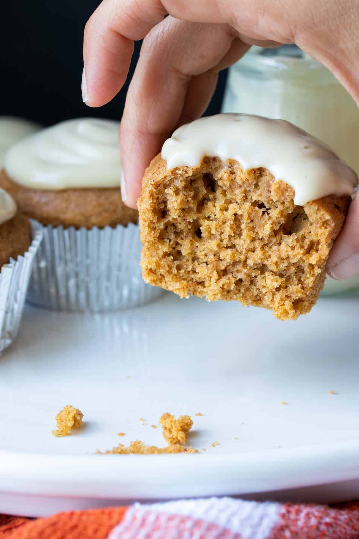 Hand picking up a half eaten pumpkin cupcake with white frosting