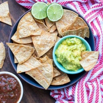 Black plate with baked tortilla chips and small bowl of guacamole