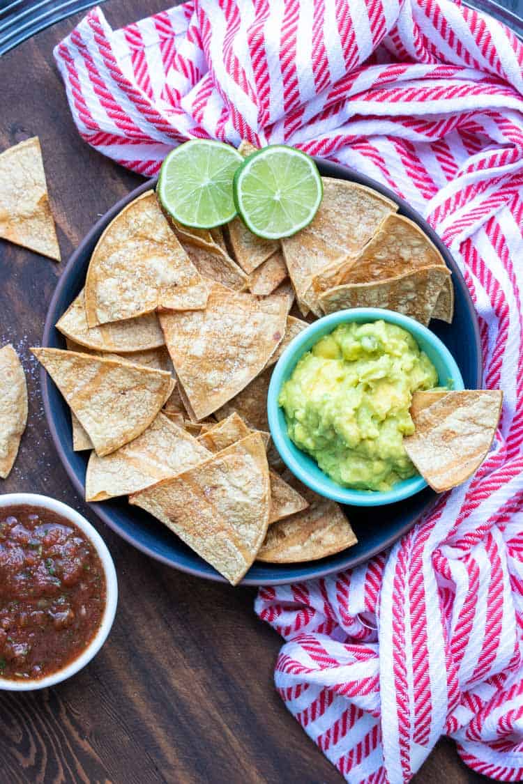 Black plate with baked tortilla chips and small bowl of guacamole