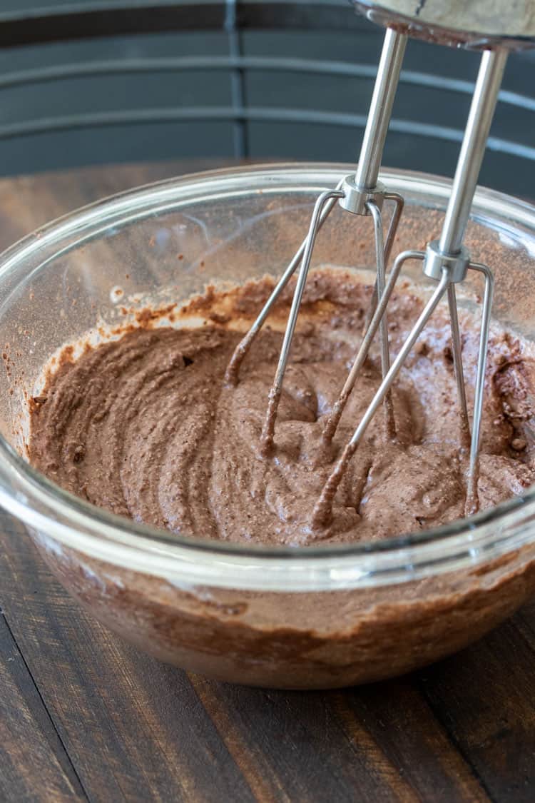 Hand mixer mixing chocolate frosting ingredients in a glass bowl