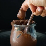 Finger taking a scoop of chocolate frosting from a glass jar