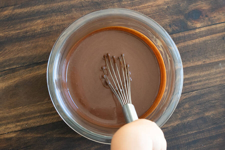 Hand mixing chocolate frosting ingredients in a glass bowl