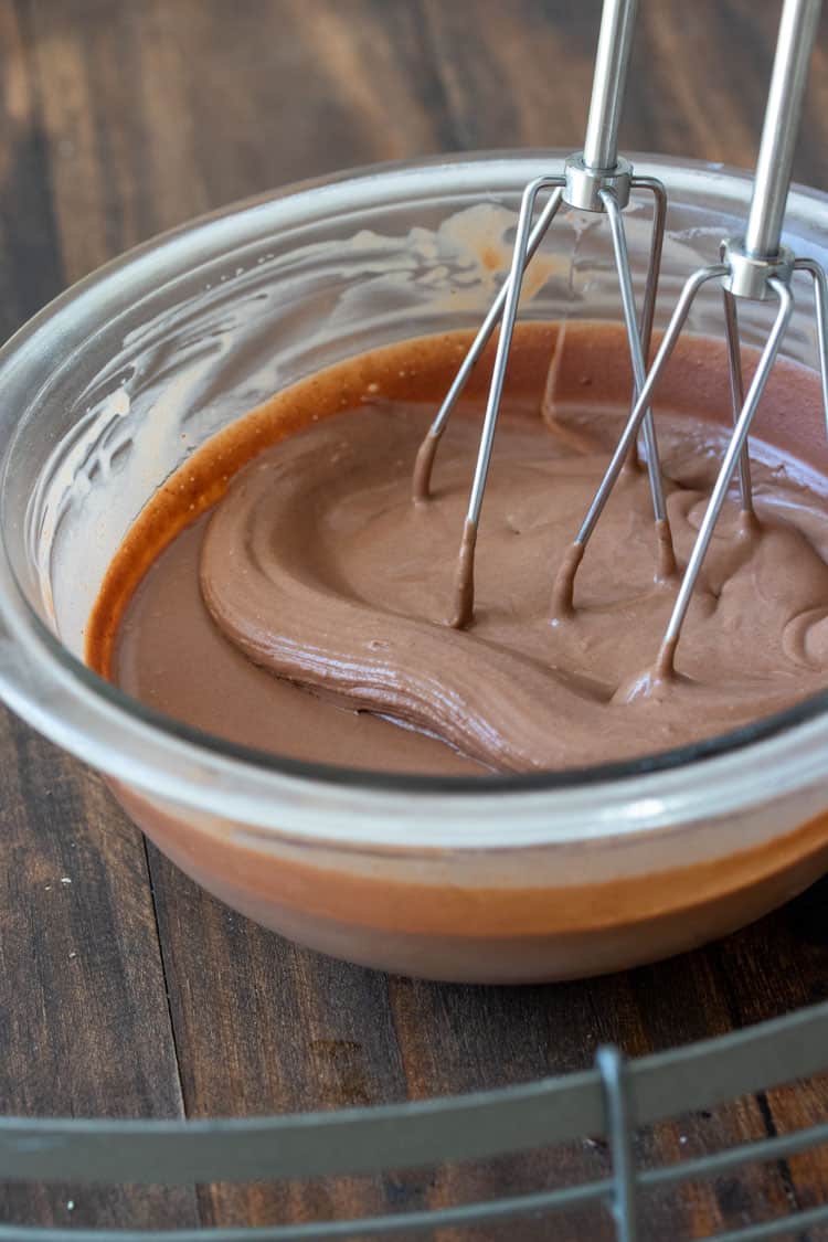 Hand mixer beating chocolate frosting in a glass bowl