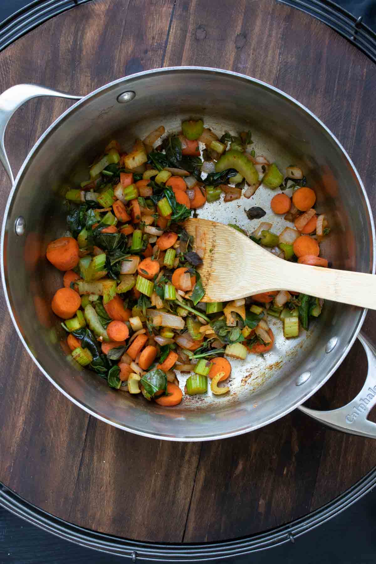 Wooden spoon mixing veggies cooking in a metal pot.