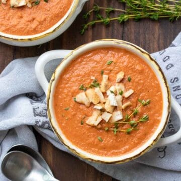 White handled soup bowls filled with creamy tomato soup and topped with crushed pretzels