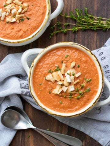 White handled soup bowls filled with creamy tomato soup and topped with crushed pretzels.