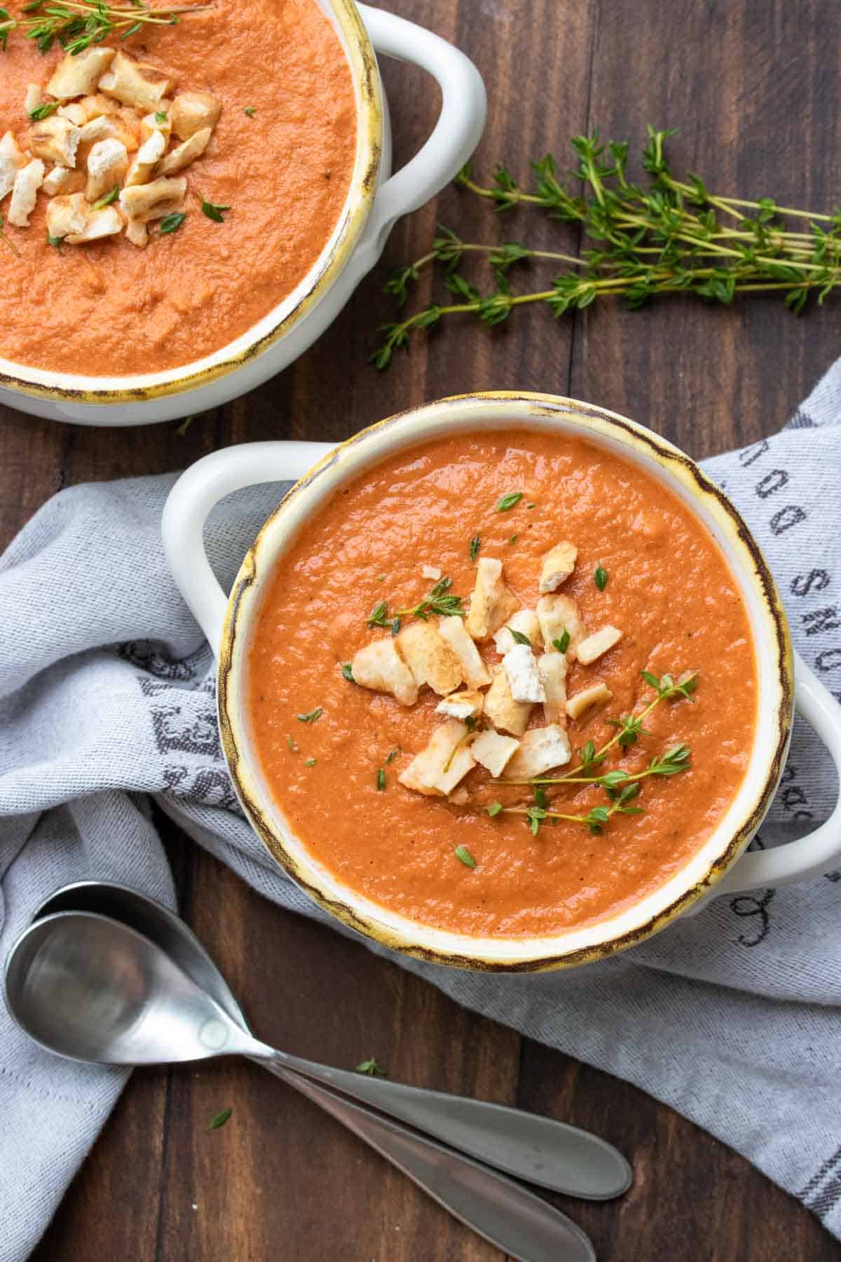 White handled soup bowls filled with creamy tomato soup and topped with crushed pretzels