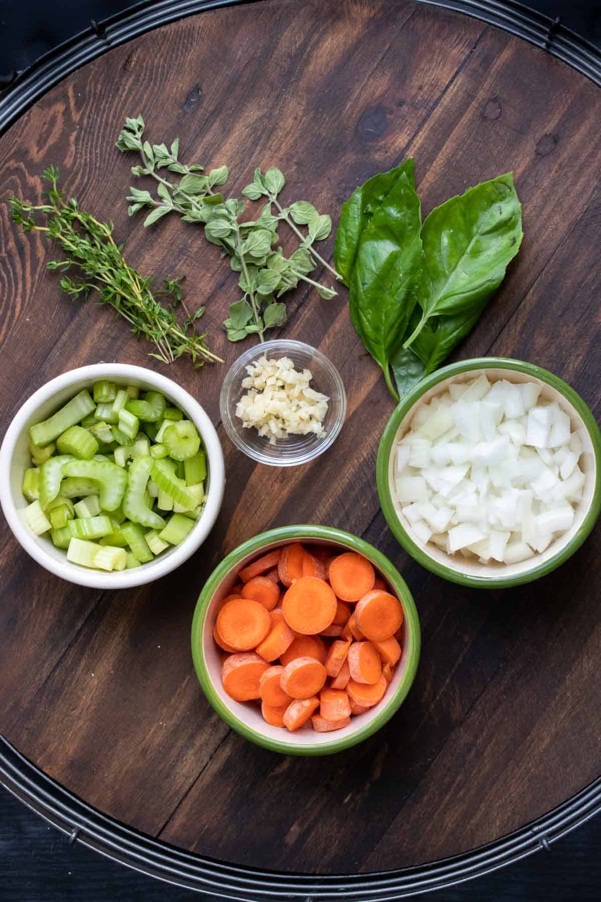 Bowls with creamy tomato soup ingredients on a wooden tray