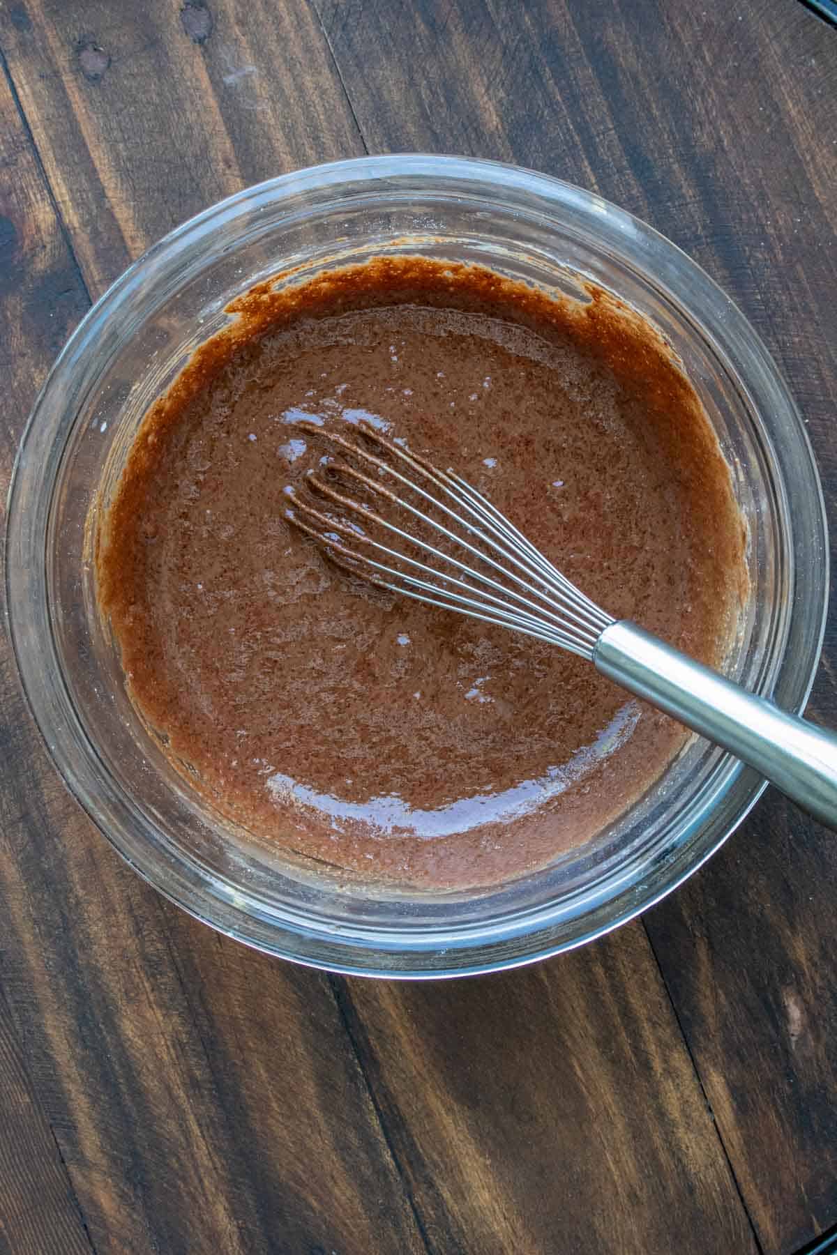 Whisk mixing chocolate cupcake batter in a glass bowl