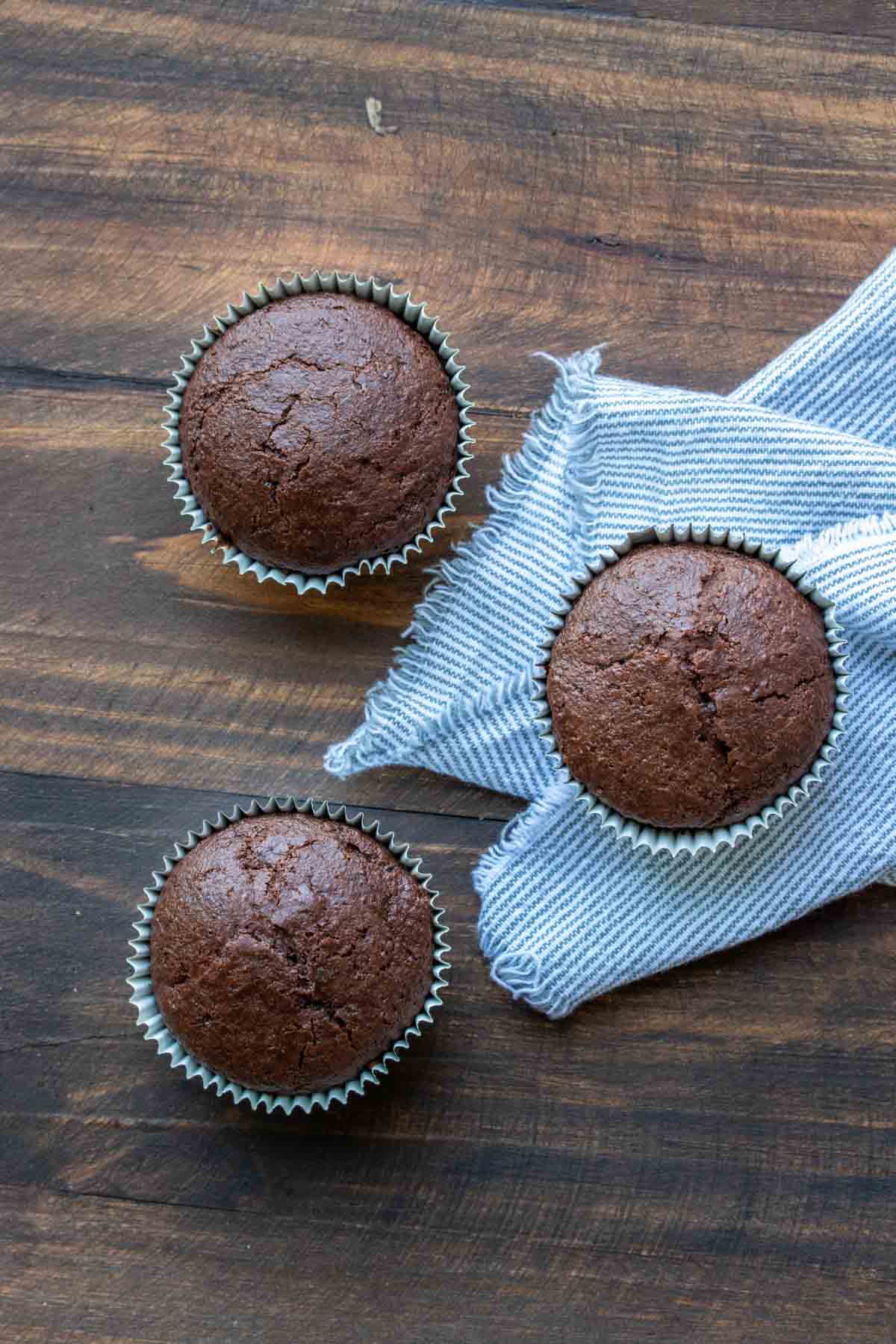 Three baked chocolate cupcakes on a wooden table