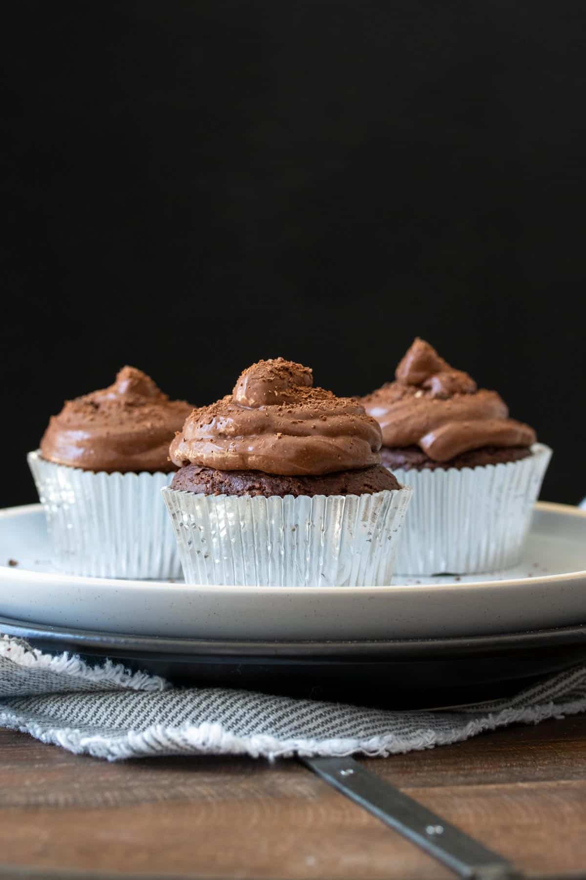 Three chocolate cupcakes with silver liners on a white plate