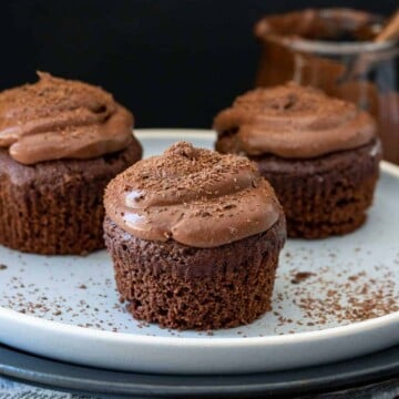 Chocolate cupcakes with chocolate frosting and no liners on a white plate