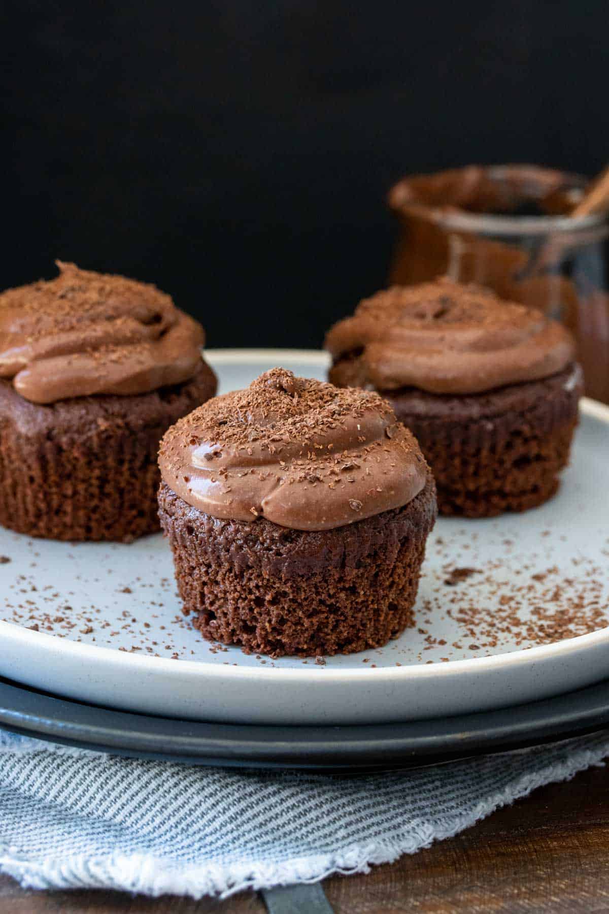 Chocolate cupcakes with chocolate frosting and no liners on a white plate