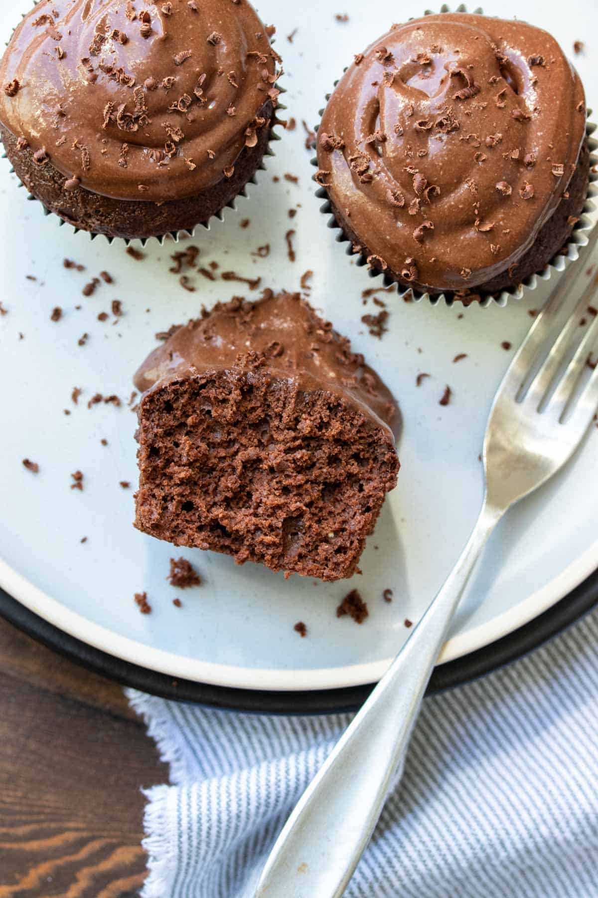 Half eaten chocolate cupcake with chocolate frosting on a white plate
