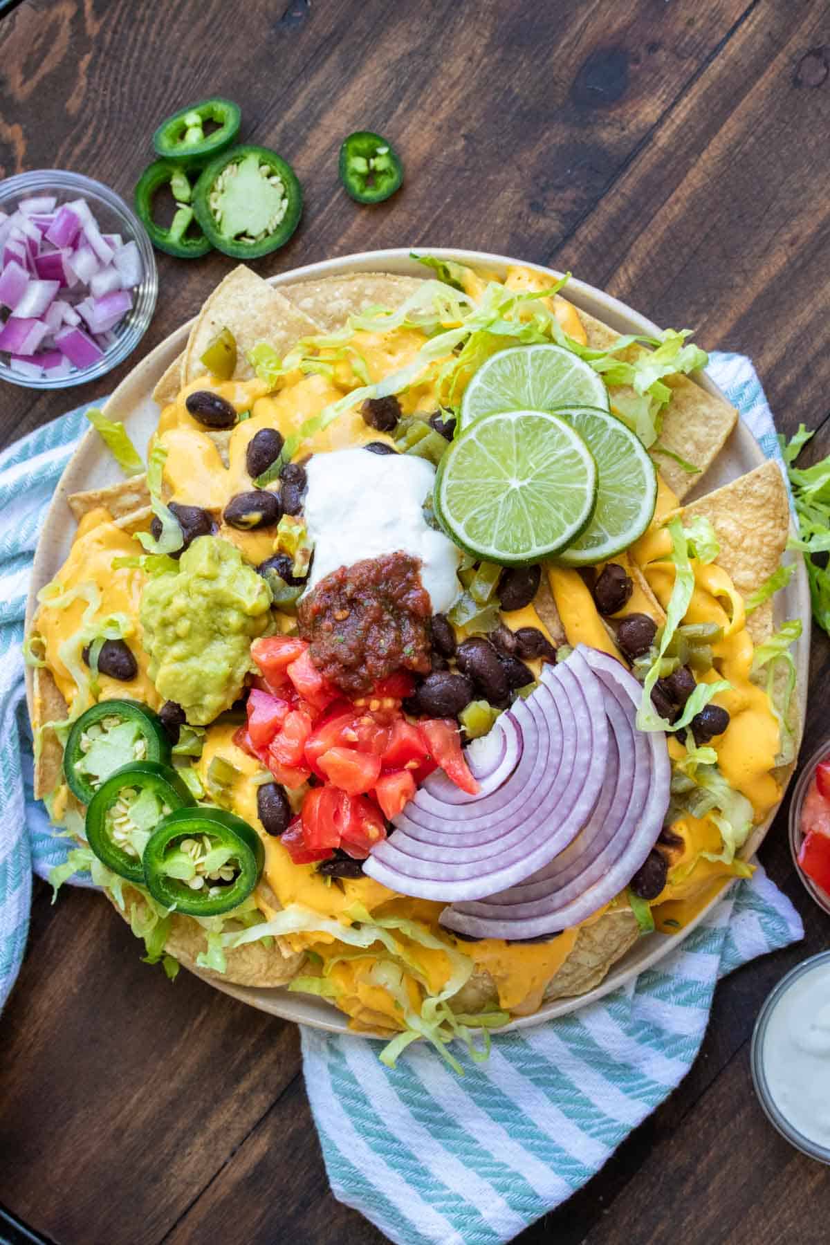 Fully loaded nachos on a tan plate resting on a striped napkin