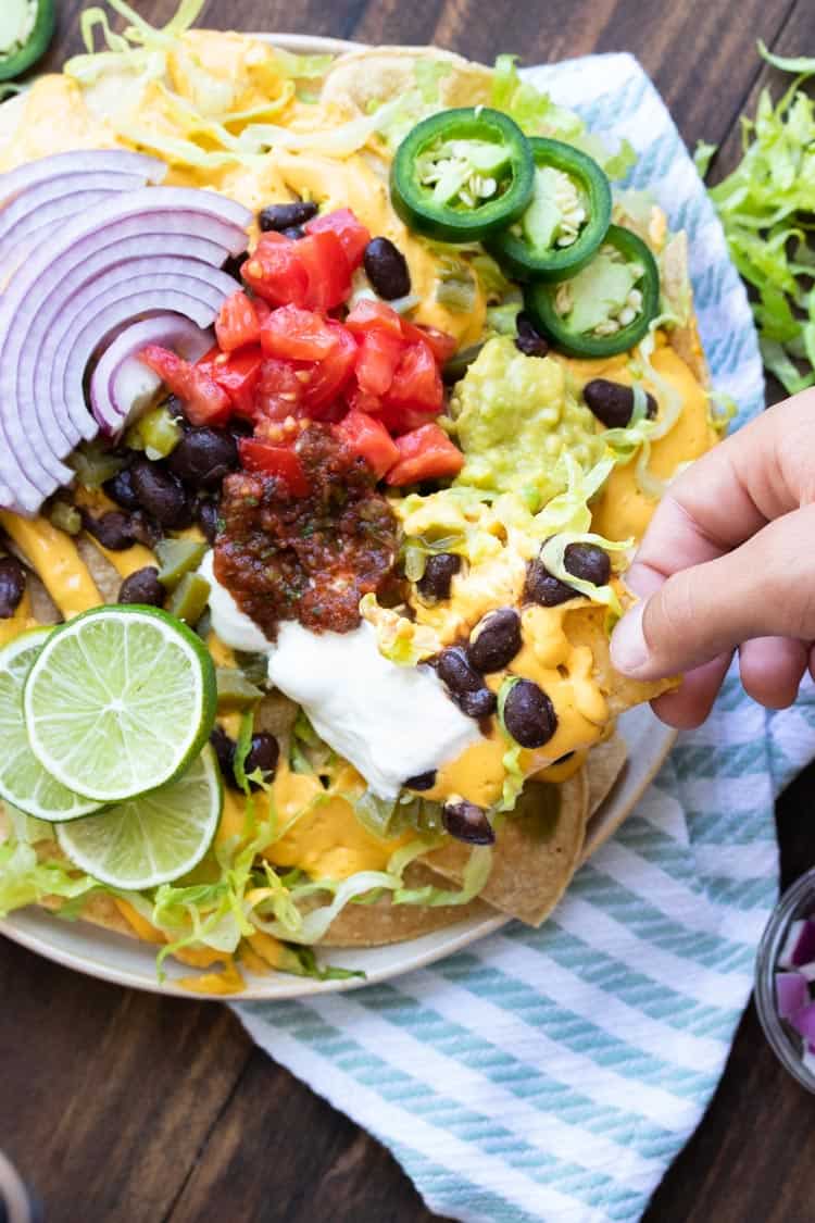 Hand picking up a nacho chip piled with cheese, beans and other ingredients.