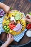 Three hands getting food from a plate of loaded nachos on a striped towel.