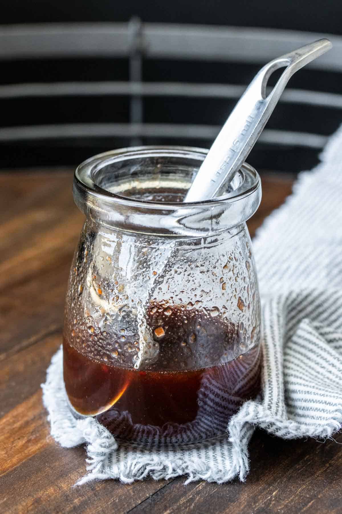 Measuring spoon in a glass bowl of maple syrup sauce.