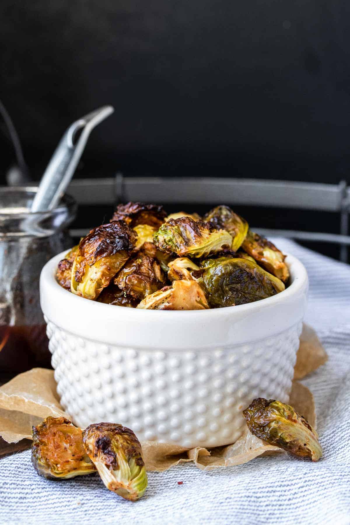 White bowl on a grey and white striped towel filled with roasted Brussels sprouts