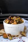 A bowl with bumps on it filled with Brussels sprouts with browned edges and sitting on a towel with some Brussels sprouts on it.