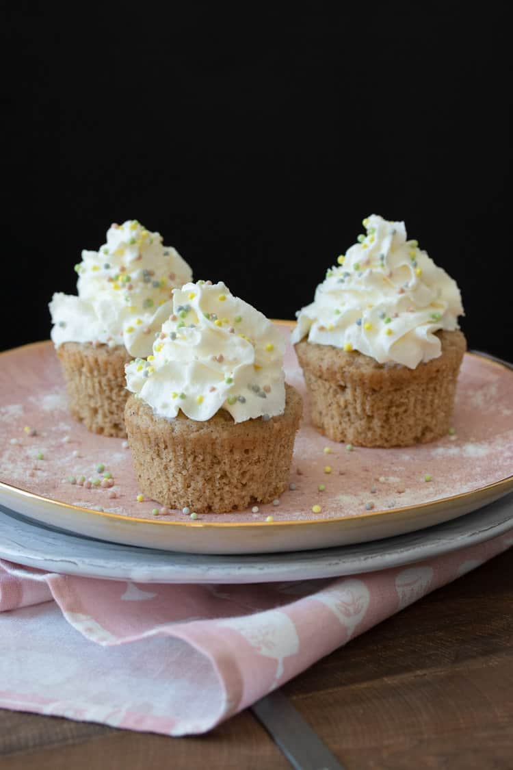 Three vanilla bean cupcakes topped with whipped cream on a pink plate