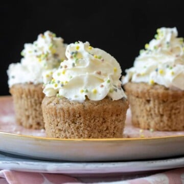 Vanilla bean cupcakes with whipped cream and sprinkles on a pink plate