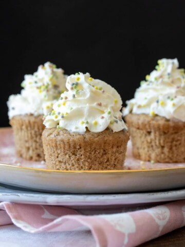 Vanilla bean cupcakes with whipped cream and sprinkles on a pink plate