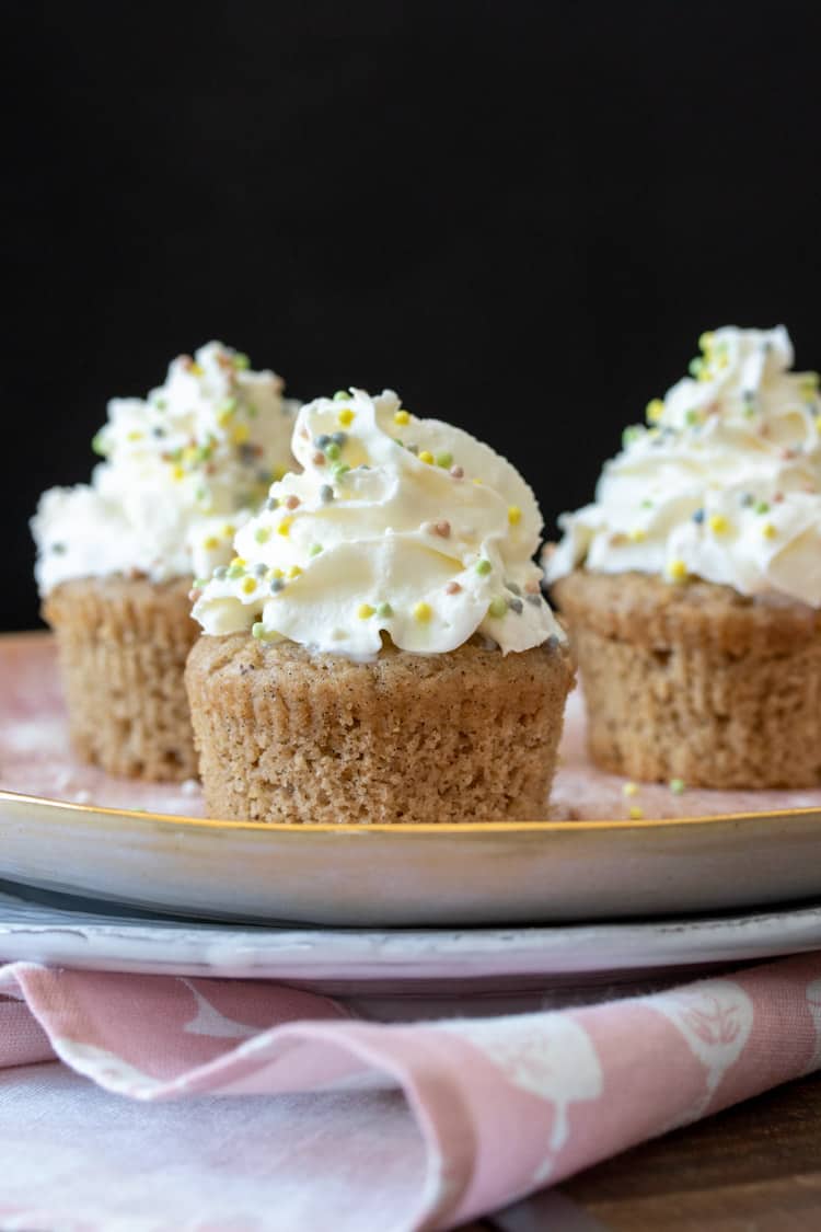 Vanilla bean cupcakes with whipped cream and sprinkles on a pink plate