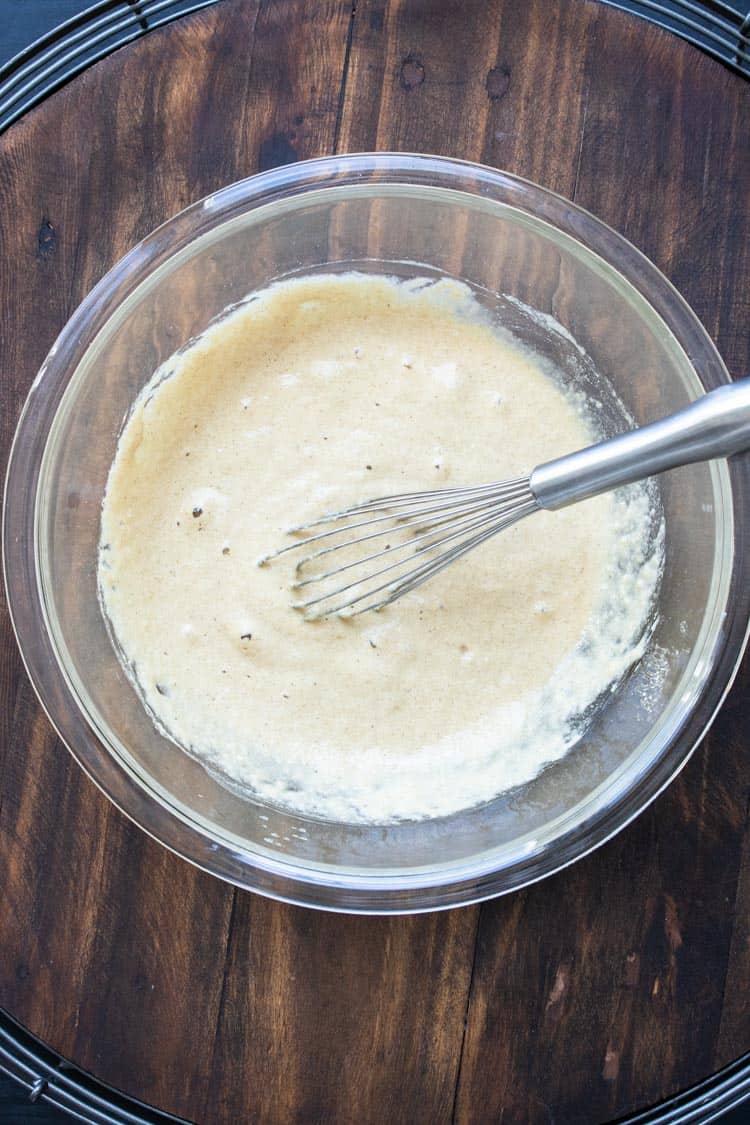 Whisk mixing vanilla cupcake batter in a glass bowl