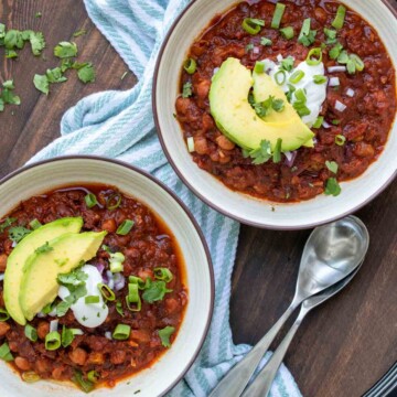 Two bowls filled with bean chili and topped with avocado slices and sour cream